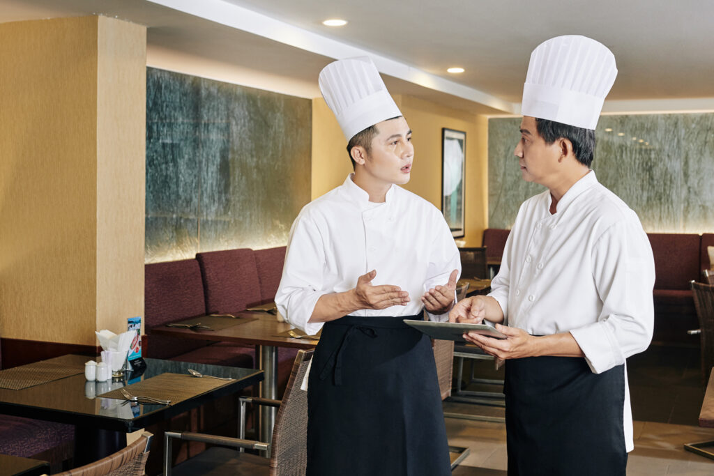 Young,Asian,Chef,In,Uniform,Explaining,Something,To,His,Colleague