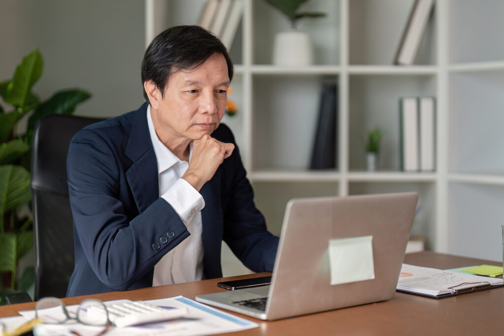 Senior financial advisor contemplating strategies while working on a laptop in a modern office