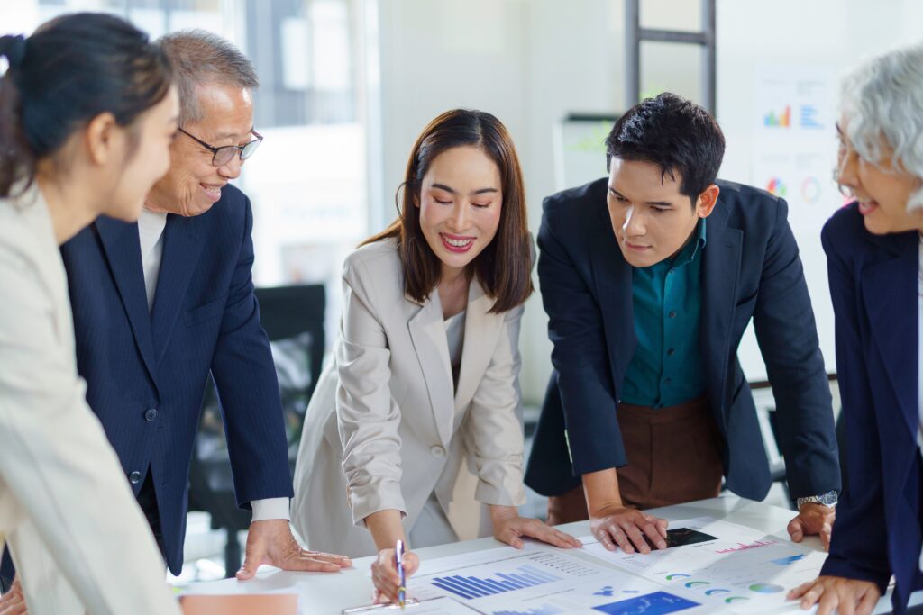 Group,Of,Asian,Businesspeople,Leaning,Over,A,Table,,Examining,Financial