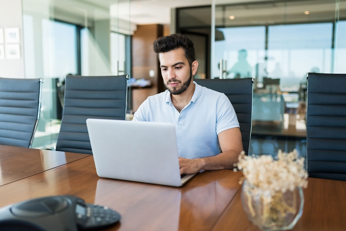 A dedicated young businessman working on laptop outside a meeting room