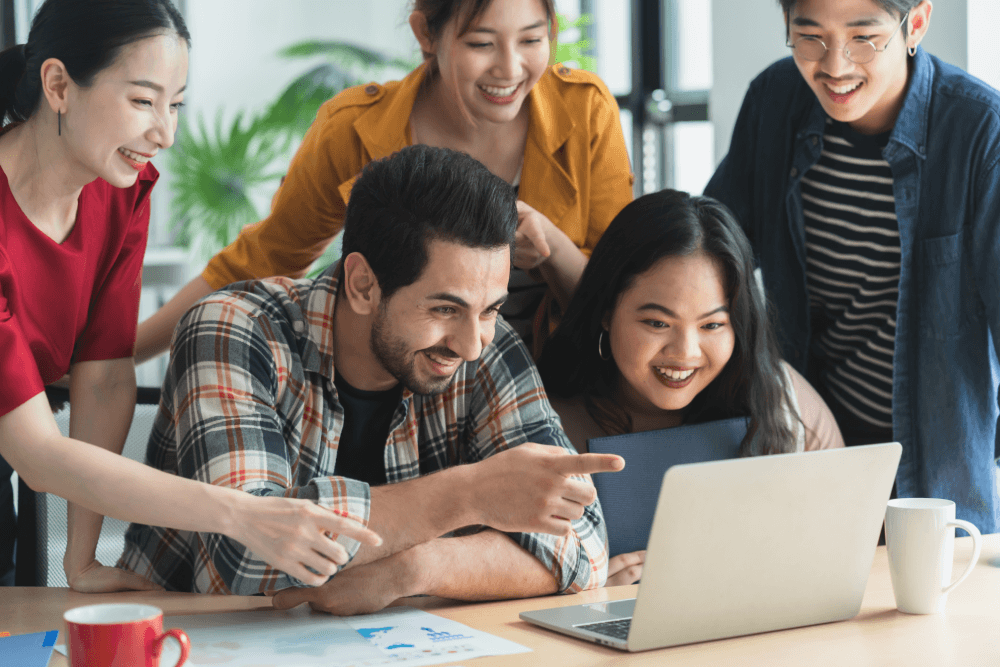 A diverse group of students working together on a laptop.