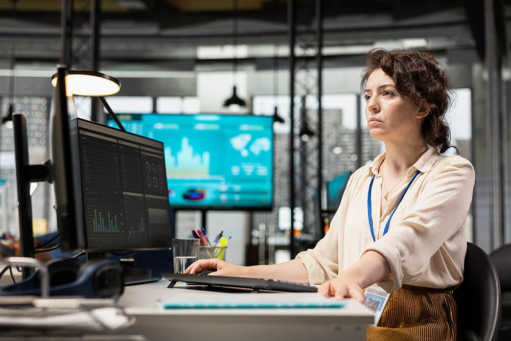A female professional sitting at a computer workstation, analyzing dark mode data dashboards and corporate metrics