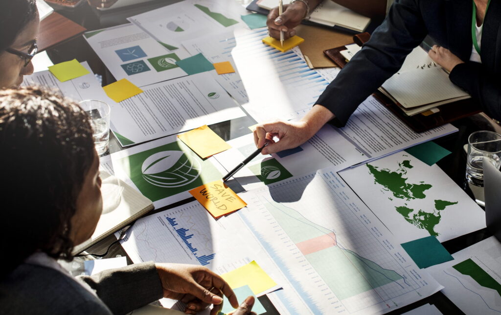 A serious, professional due diligence meeting where team members review complex financial models, metrics, and forecasting diagrams to evaluate impact investment opportunities