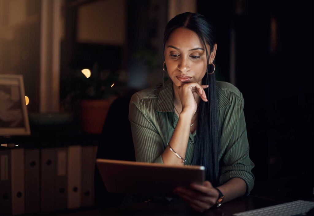 Professional woman taking an online class on a tablet in a dimly lit office during late hours.